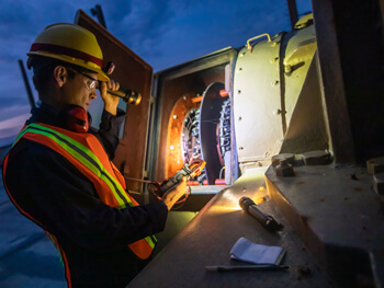 Technician wearing safety gear working with a flashlight at night assessing equipment
